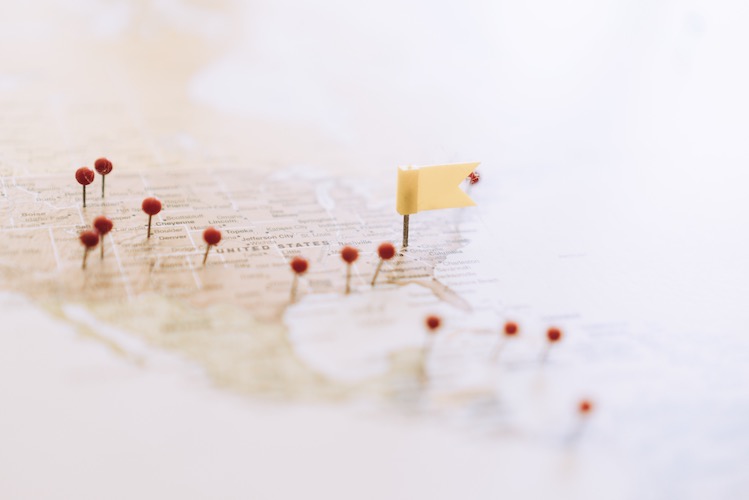 A close-up view of a map of the United States with red pins marking various locations and a small yellow flag highlighting a specific destination.